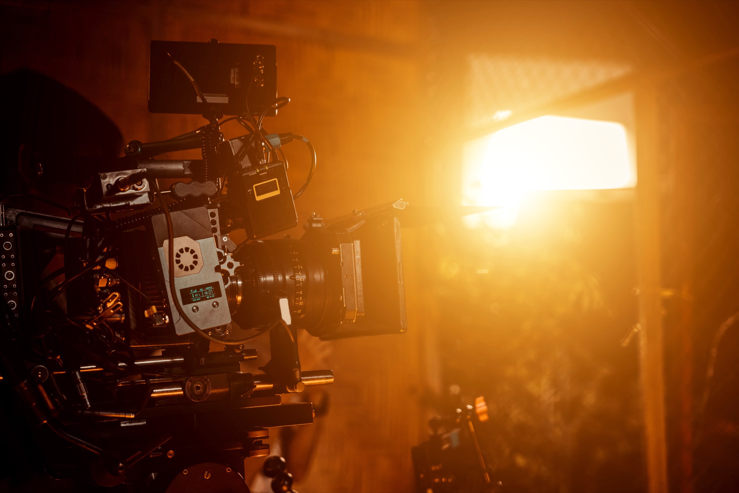 A cinema camera on a film set, backlit by a warm key light